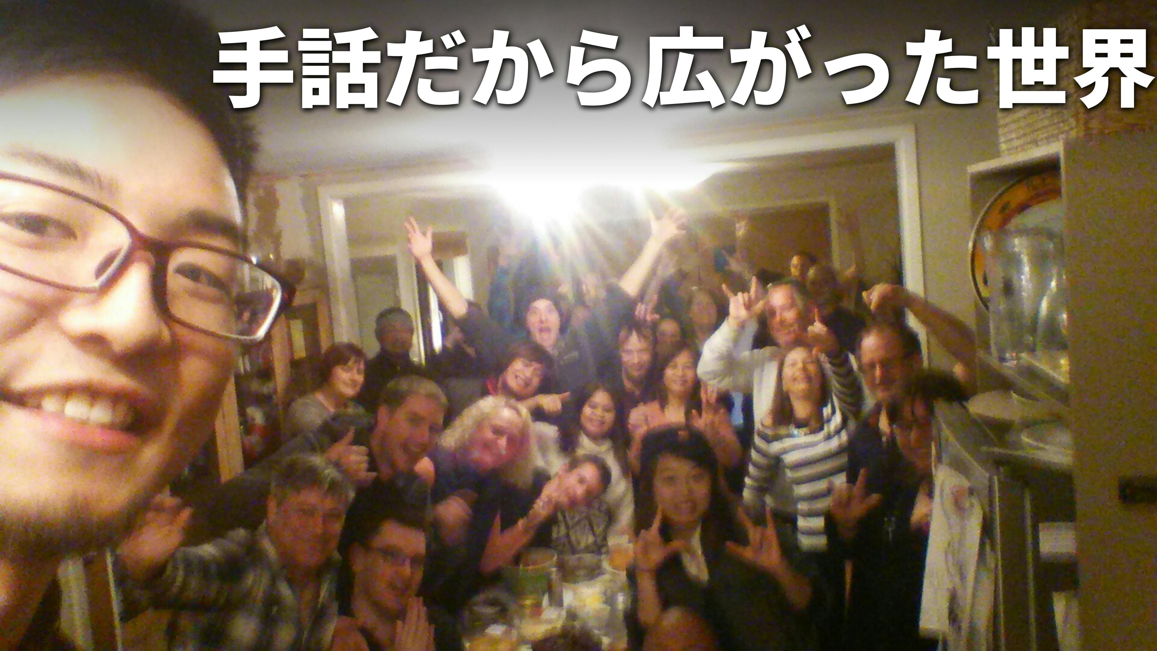 竹花がニュージーランドでホームパーティをした時に撮影した集合写真。老若男女の30人ほど写っている写真を背景に、白文字で「手話だから広がった世界」