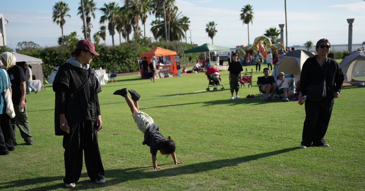西宮市で開催された野外イベントにて、楽しくなってしまって芝生の上で倒立をする子どもの写真。青空と芝生と会場の緩やかな雰囲気が映し出されています。