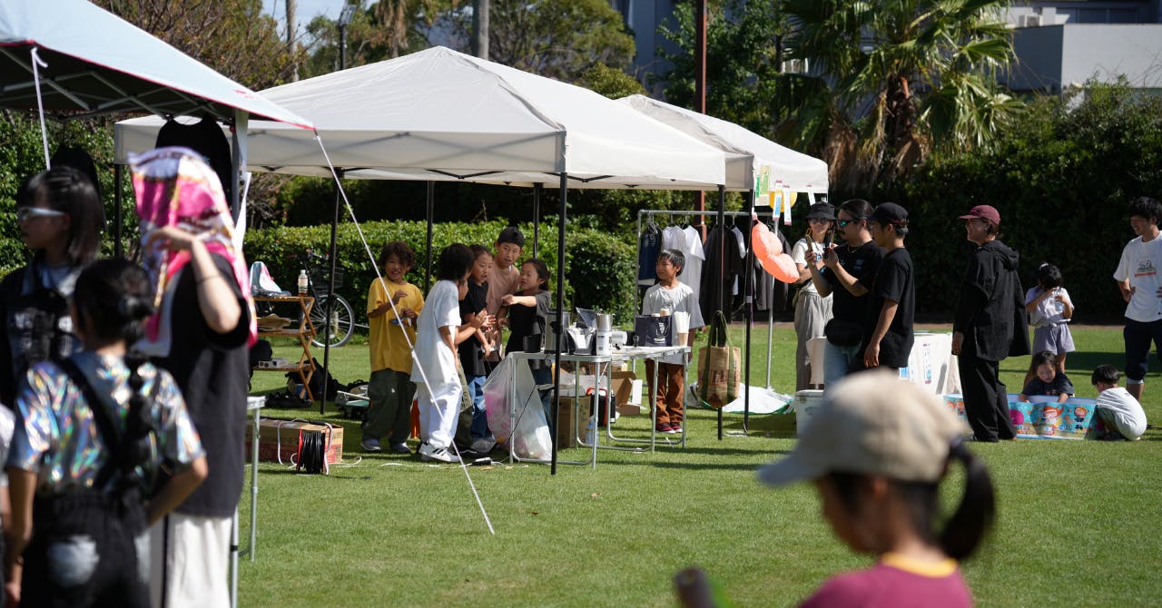 西宮市で開催された野外イベントにて、会場の雰囲気が映し出されています。真ん中のテントで子どもたちが店番をしています。