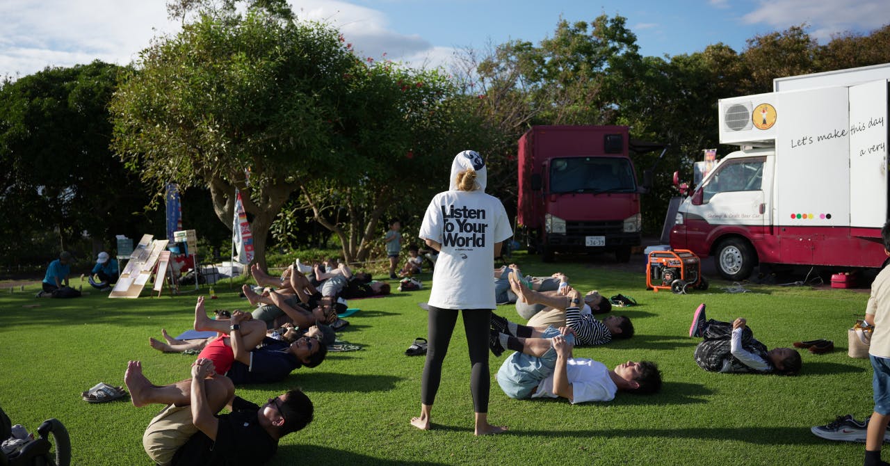 西宮市の野外イベントにて芝生の上で数名の大人がヨガをしています。真ん中には先生が立っています。